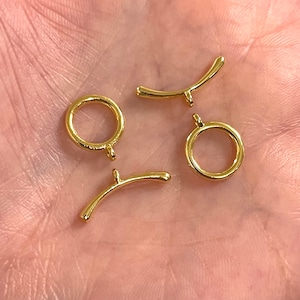 Puede incluir: Cuatro hallazgos de joyería de metal dorado, incluyendo dos anillos de salto y dos conectores curvos.