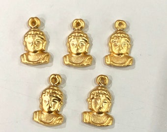 May include: Five gold-colored metal charms featuring a Buddha head design. Each charm has a loop at the top for attaching to a necklace or bracelet.