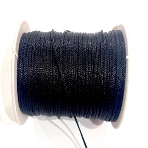 May include: A black cord wound onto a white spool. The cord is a deep, solid black, and appears to be made of a smooth, possibly synthetic material. The spool has white sides and a central core, providing a clean contrast to the dark cord. Ideal for crafts.
