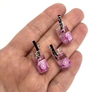 Peut inclure: Trois petits pots en verre avec des pailles noires et des couvercles argentés remplis d'un liquide rose et de tranches d'oignons rouges.