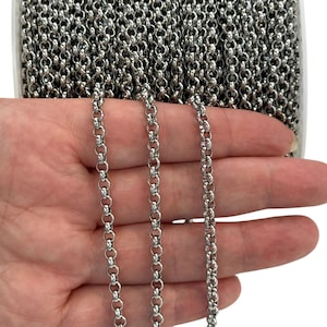 Könnte beinhalten: Nahaufnahme einer Rolle silberfarbener Kette. Die Kette besteht aus kleinen, runden Gliedern, die eine strukturierte Oberfläche bilden. Die Kette wird in der Hand einer Person gehalten, wobei die Kette über die Finger herabfällt.