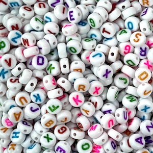 Peut inclure: Un grand nombre de perles d'alphabet en plastique blanc avec des lettres colorées. Les perles sont toutes de la même taille et de la même forme, et elles sont disposées de manière aléatoire.