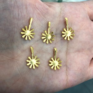 May include: Five gold-coloured metal charms in the shape of a flower with a loop at the top for attaching to jewellery.