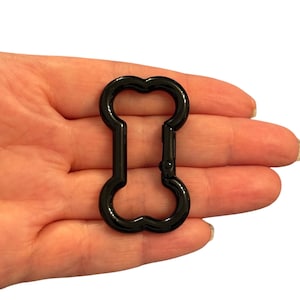 May include: A black metal swivel clasp in a bone shape. The clasp is held open, revealing the spring-loaded mechanism. The clasp is approximately 7.6 cm long.