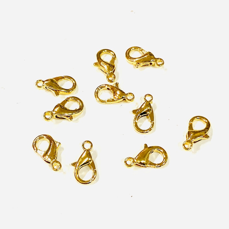 May include: A group of ten gold-toned lobster clasps, a type of jewelry finding used for attaching chains or cords to jewelry pieces.