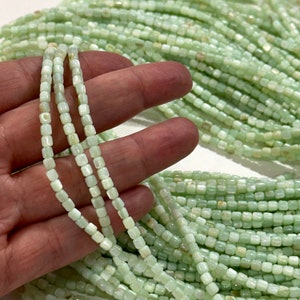 May include: A strand of light green square-shaped beads made from shell. The beads have a slight iridescent sheen.