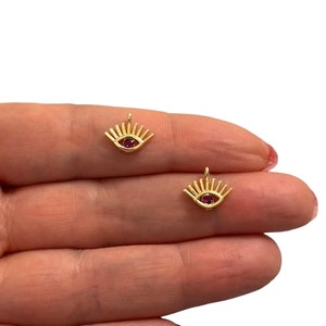 May include: Two gold evil eye charms with red gemstone centres. The charms are small and delicate, perfect for adding a touch of protection and style to jewellery.