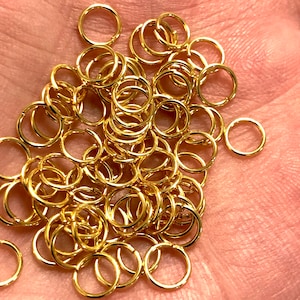 May include: A pile of gold jump rings, a type of jewellery finding used for connecting chains, cords, and other jewellery components.