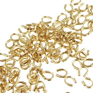 May include: A large pile of gold-colored metal jump rings. The rings are small and have a rounded shape.