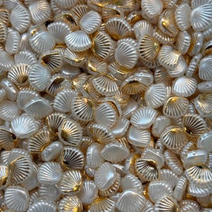 Peut inclure: Gros plan sur un tas de perles en forme de coquillage. Les perles sont un mélange de blanc et d'or, avec un éclat nacré. Les perles dorées ont une finition métallique et les perles blanches sont opaques. Idéal pour la création de bijoux et les projets d'artisanat.