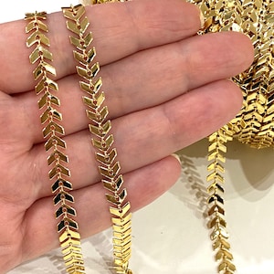 Könnte beinhalten: Goldene Kettenborte mit Chevron-Muster. Die Kette besteht aus kleinen, miteinander verbundenen Pfeilformen.