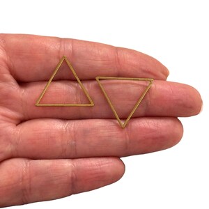 Puede incluir: Dos marcos de metal de forma triangular de color dorado. Los marcos están abiertos y se pueden utilizar para manualidades.