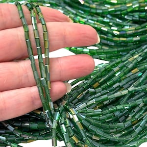 Könnte beinhalten: Eine Strähne grüner Glasperlen mit irisierendem Finish. Die Perlen sind rechteckig und haben einen leichten Schimmer.