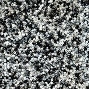 May include: A close-up view of a pile of small, round beads in various shades of black, white, and gray. The beads are scattered, creating a textured surface. These beads are suitable for jewelry making and craft projects.
