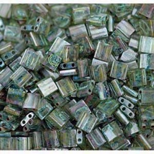 Puede incluir: Un montón grande de pequeñas cuentas cuadradas de vidrio verde iridiscente. Las cuentas tienen una forma ligeramente irregular y un brillo metálico.
