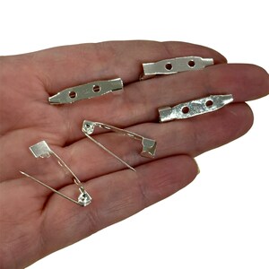 May include: Silver-colored brooch backs and pin backs. The brooch backs have two or three holes for attaching to fabric. The pin backs have a safety pin style clasp. These are ideal for crafting and jewelry making.