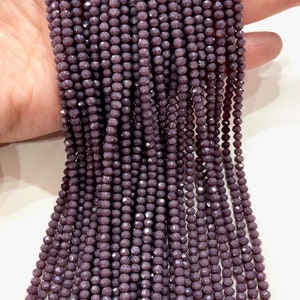 Può includere: Un filo di perline di vetro sfaccettate di colore viola scuro. Le perline sono piccole e di dimensioni uniformi, creando un aspetto liscio ed elegante.