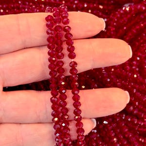 Może przedstawiać: Sznur czerwonych fasetowanych koralików szklanych. Koraliki są małe i mają błyszczące wykończenie.