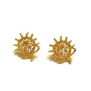 May include: A pair of gold-toned earrings with a circular design that resembles a sun or a wheel. The earrings are made of a delicate, intricate rope-like material.