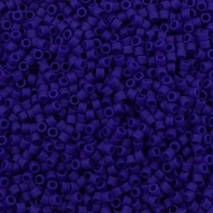 May include: A close-up view of a large quantity of small, round, opaque purple beads. The beads are all the same size and shape, and they are arranged in a random pattern.
