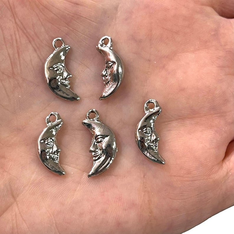 May include: Five silver crescent moon charms with a face on each. The charms have a loop at the top for attaching to jewelry or other crafts.