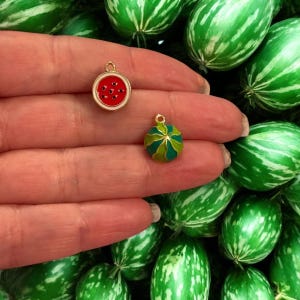 Puede incluir: Dos abalorios de color dorado, uno con forma de sandía con detalles rojos y negros, y el otro con forma de melón rayado verde y amarillo.