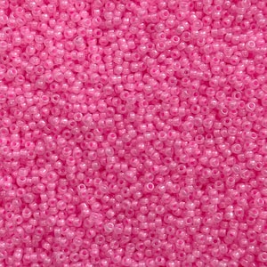 Puede incluir: Primer plano de un montón de pequeñas cuentas de semillas rosas translúcidas. Las cuentas están densamente empaquetadas, creando una superficie texturizada. El color es un rosa vibrante y brillante, y las cuentas parecen ser de vidrio o plástico.