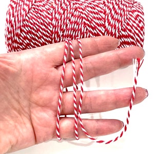 May include: Red and white baker's twine, a type of string used for wrapping and tying, is shown in a close-up image. The twine is made of natural fibres and has a rustic look.