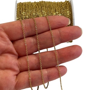 May include: A spool of gold-coloured chain, approximately 18 inches long, is held in a hand. The chain is made of small, linked metal pieces.