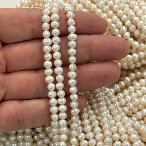 Pode incluir: Uma coleção de pequenas pérolas de água doce em tom branco-sujo com um acabamento lustroso. As pérolas têm uma forma redonda a ligeiramente oval e estão dispostas em vários fios, exibindo a sua textura natural e cor creme consistente.