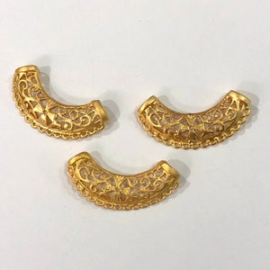 Puede incluir: Tres piezas decorativas de metal de color dorado con un intrincado diseño floral. Las piezas tienen forma de media luna y presentan un delicado patrón calado.