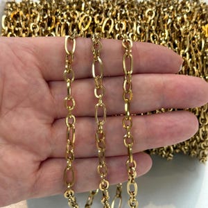 May include: A gold-toned metal chain featuring a repeating pattern of elongated oval links and smaller circular links. The chain has a polished, reflective surface and is presented as a continuous length of jewellery-making material.