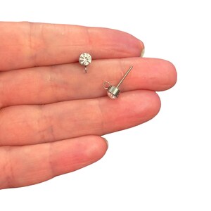 以下が含まれることがあります： 金属製のベゼルにセットされた透明で丸いファセットカットのクリスタルが付いた、シルバーカラーのスタッドピアス用パーツ2点。各スタッドのベース部分には、チャームや飾りを吊り下げるための小さな円形のループが付いています。