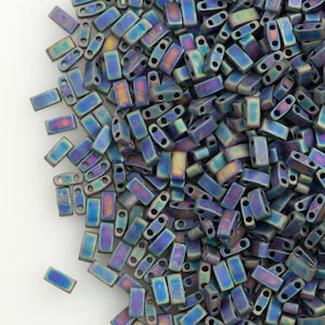 May include: A large pile of iridescent blue and purple seed beads. The beads are small and rectangular with two holes in each bead.