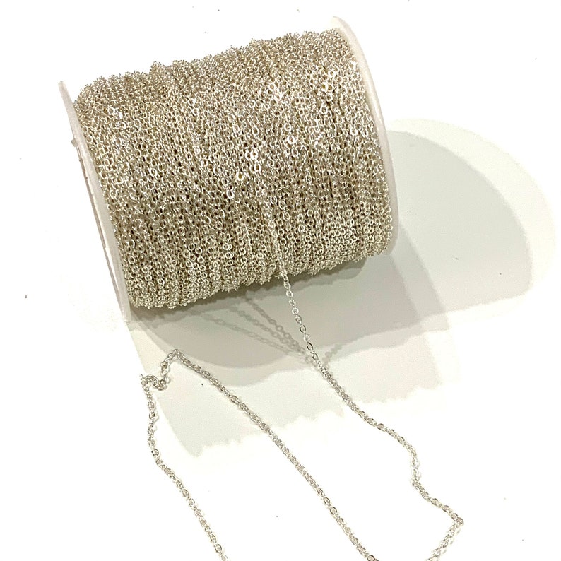 May include: A spool of silver chain, with a length of chain extending from the spool. The chain is a fine, delicate chain.