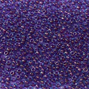May include: A close-up view of a large quantity of small, round, iridescent purple beads. The beads have a light blue sheen.