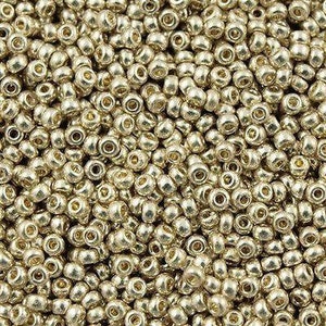 Puede incluir: Una vista de cerca de una gran cantidad de pequeñas cuentas redondas de color dorado metálico. Las cuentas tienen un acabado liso y brillante y son perfectas para la elaboración de joyas o proyectos de manualidades.