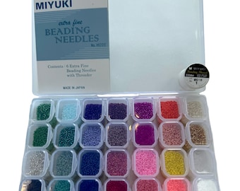 May include: A clear plastic organizer filled with small, colorful beads in various shades. The organizer is open, revealing individual compartments of beads. A package of Miyuki extra fine beading needles is on top, with text that reads "extra fine BEADING NEEDLES".