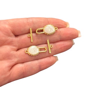 May include: Four gold-tone toggle clasps with white glitter accents. Each clasp has a round, decorative top with a scalloped edge.
