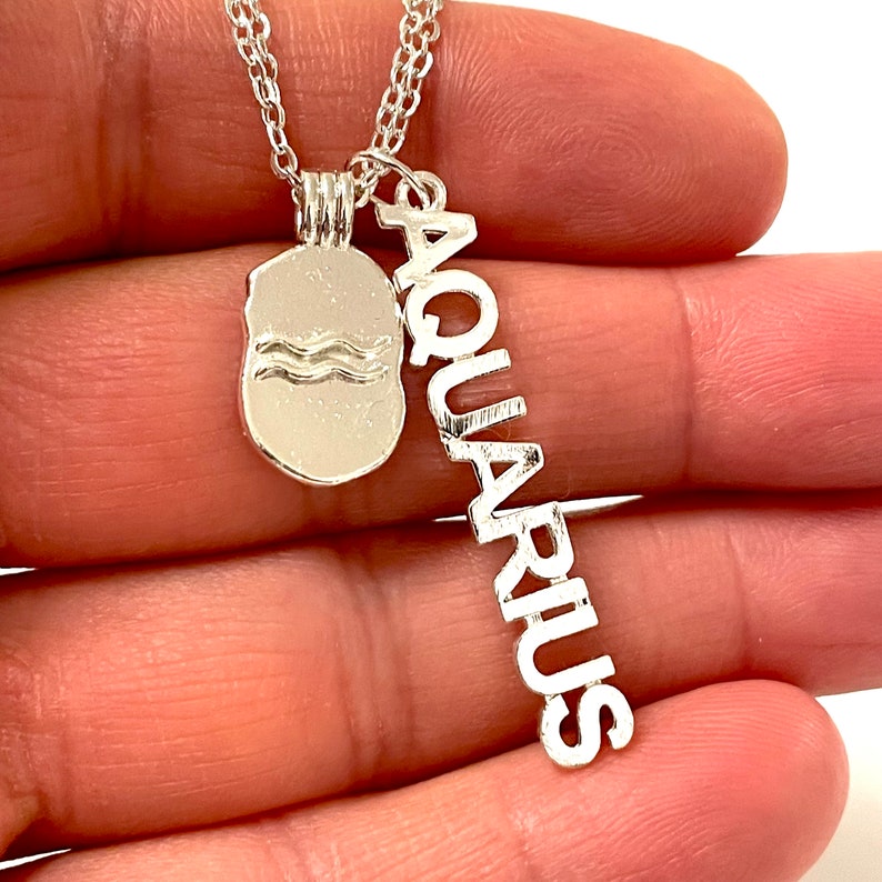 May include: Silver necklace with a charm featuring the Aquarius zodiac symbol and the word "Aquarius" spelled vertically.