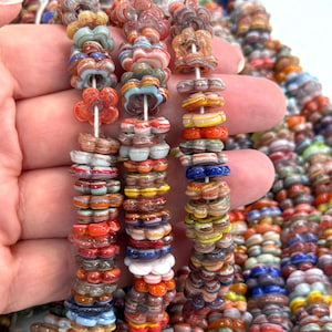 以下が含まれることがあります： 赤、オレンジ、黄色、青、白など、さまざまな色の花型のガラスビーズのストランドのクローズアップ。ビーズは一緒にひもでつながれており、質感と鮮やかな外観を作り出しています。ジュエリー作りや工芸に最適です。