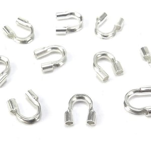 Puede incluir: Diez cuentas de crimp de plata, también conocidas como tubos de crimp, se muestran sobre un fondo blanco. Estas cuentas se utilizan para asegurar los hallazgos de joyería y crear un acabado profesional.