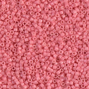 May include: A close-up image of a large quantity of small, pink, round seed beads. The beads are all the same size and shape, and they are arranged in a random pattern.