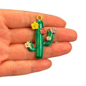 May include: A green cactus-shaped pendant featuring a metallic finish and five small, colourful flowers in yellow, pink, light blue, and white. The pendant includes a gold-toned circular loop at the top for attachment, showcasing a vibrant design.