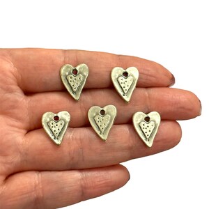 May include: Five silver metal heart-shaped charms with a textured surface and a small hole at the top for hanging.