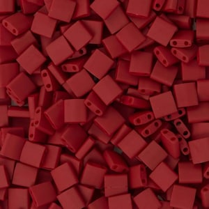 Puede incluir: Una imagen de primer plano de un montón de pequeñas cuentas cuadradas de color rojo. Las cuentas tienen dos agujeros en cada lado.