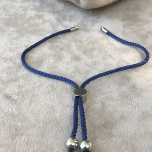 May include: A blue cord bracelet with silver metal accents. The bracelet has a sliding knot closure and two silver beads at the end.