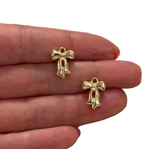 May include: Two gold-colored metal bow charms with a loop at the top for attaching to jewelry or crafts.