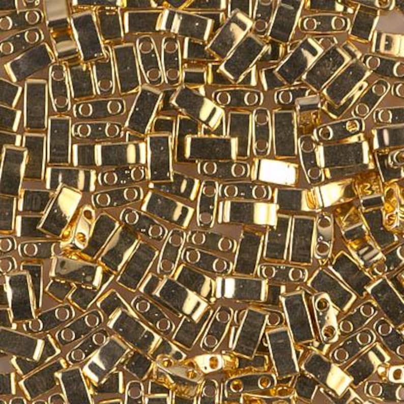 May include: A large quantity of gold-colored metal beads, each with two holes. The beads are rectangular in shape and have a smooth, shiny finish.