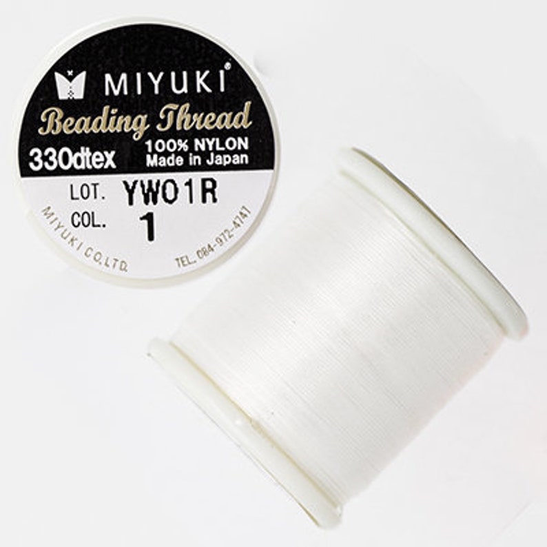 Pu&ograve; includere: Bobina bianca di filo per perline Miyuki, 330dtex, 100% nylon, made in Japan. L'etichetta riporta "LOT. YWO1R COL. 1".